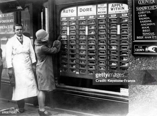 Jeune femme utilise le distributeur automatique de denrées alimentaires sous le regard vigileant de l'épicier, à Londres, Royaume-Uni.