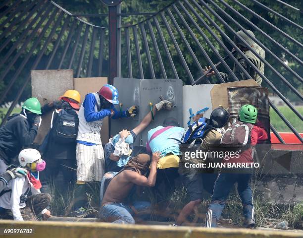 Venezuelan opposition activists attempt to defilade behind a wall from a National Guard riot policeman shooting rubber bullets at them during clashes...