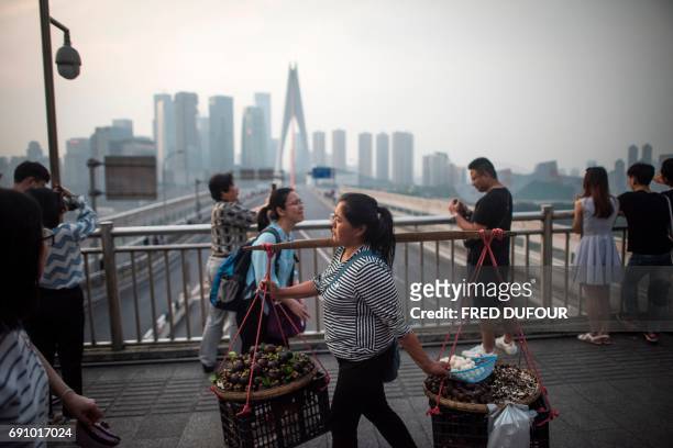Woman carries food to sell as tourists enjoy the view of the Yangtze river in Chongqing on May 31, 2017. / AFP PHOTO / FRED DUFOUR