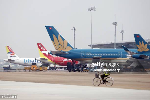 Member of the ground staff rides a bicycle past Vietnam Airlines JSC, right, Vietjet Aviation JSC, center, and BH Air aircraft at Tan Son Nhat...