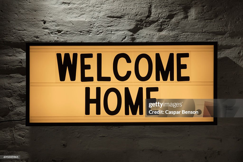 Close-up of Welcome Home signboard against gray wall