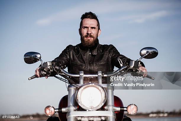portrait of confident biker sitting on motorcycle against sky - front view stock pictures, royalty-free photos & images