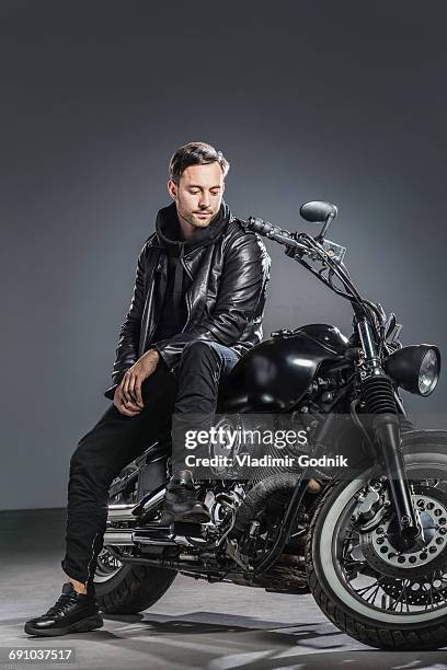 full length of man sitting on motorcycle against gray background - motorcycle rider stock pictures, royalty-free photos & images