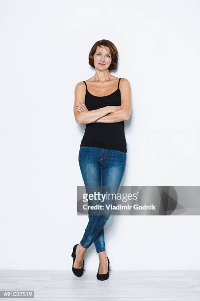 full length portrait of confident woman standing arms crossed against white background - white jeans fotografías e imágenes de stock