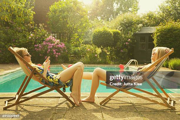 side view of female friends relaxing on deck chairs at poolside during summer - feet on table stock pictures, royalty-free photos & images