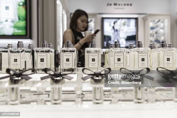 Customer uses a smartphone behind bottles of fragrance on display at a Jo Malone Ltd. Store in the Raffles City shopping mall in Shanghai, China, on...