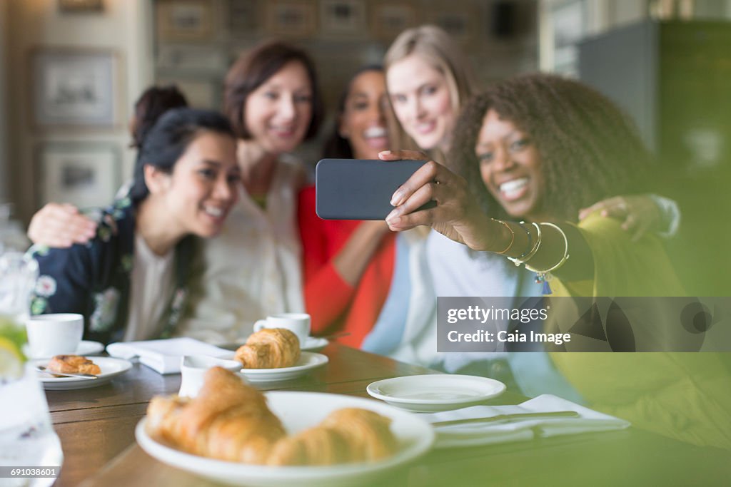 Smiling women friends taking selfie with camera phone in restaurant