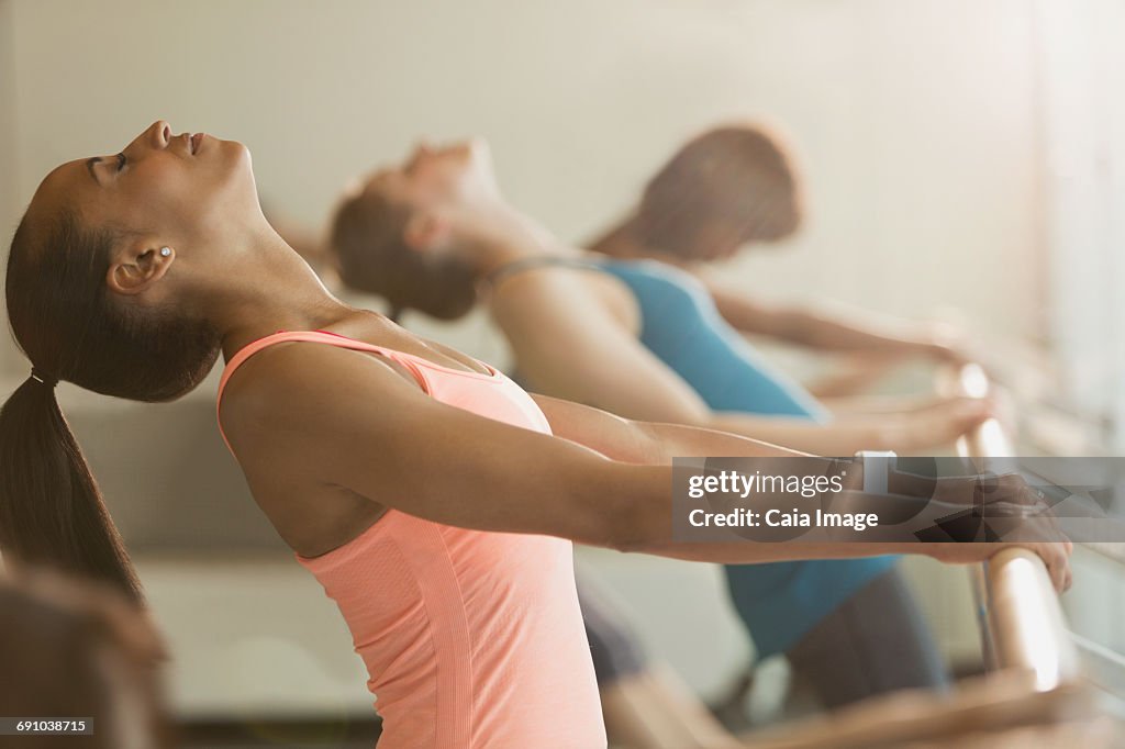 Women stretching in backbend at barre in exercise class gym studio