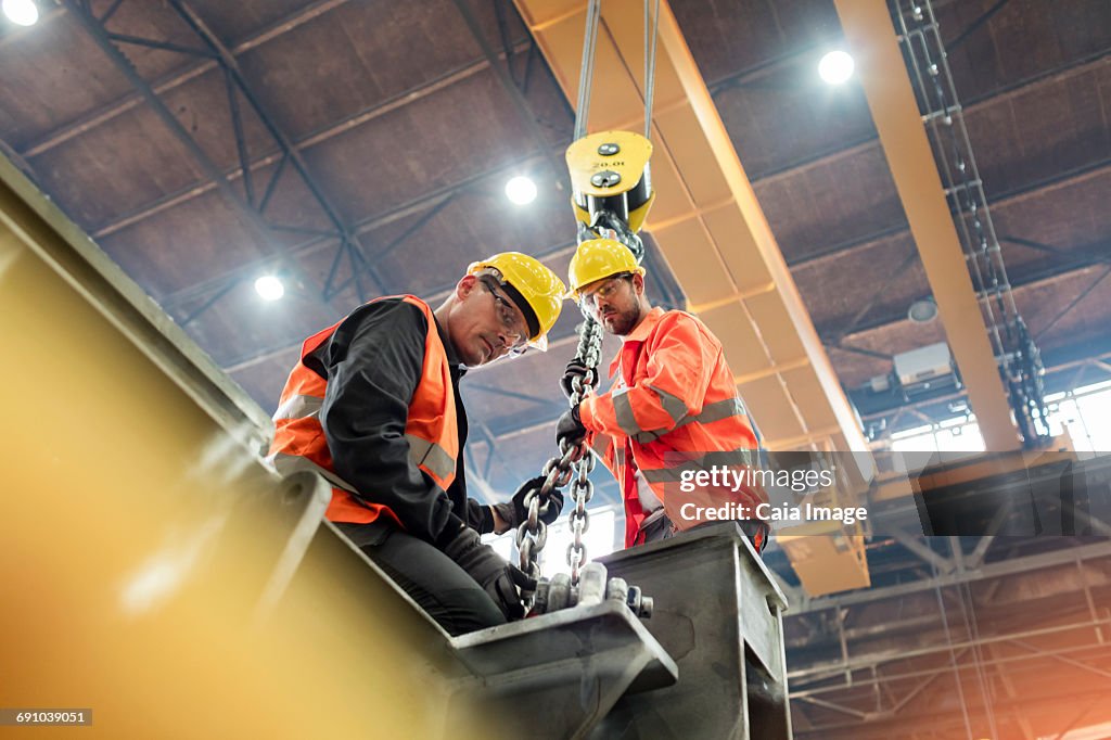 Steel workers fastening steel to crane in factory