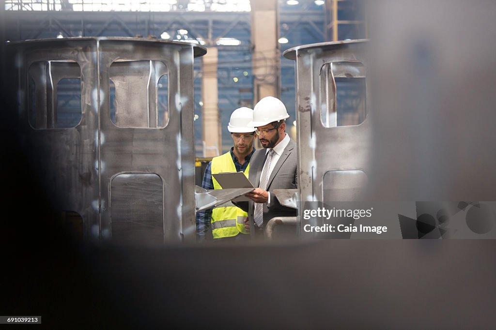 Manager and steel worker with clipboard meeting in factory