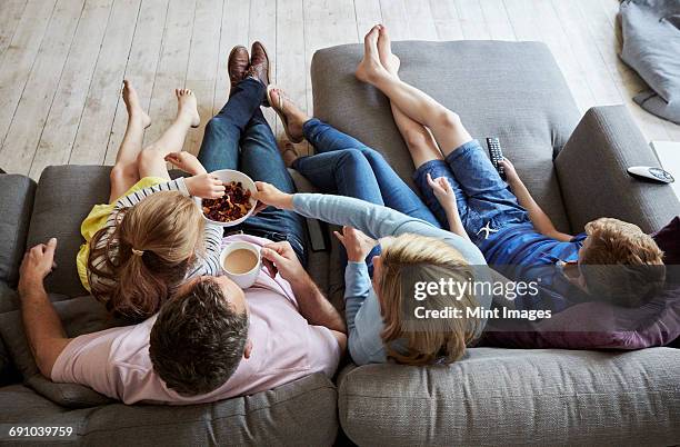 a family at home. view from above of two adults and two children seated on a sofa together. - family in front of tv stock pictures, royalty-free photos & images