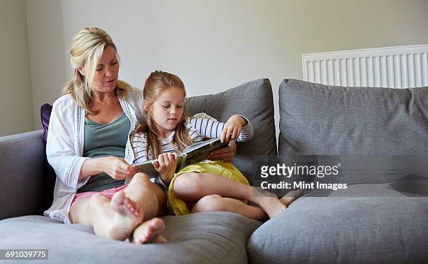 a family home. a mother and daughter sitting on the sofa reading a book. - donne bionde scalze foto e immagini stock