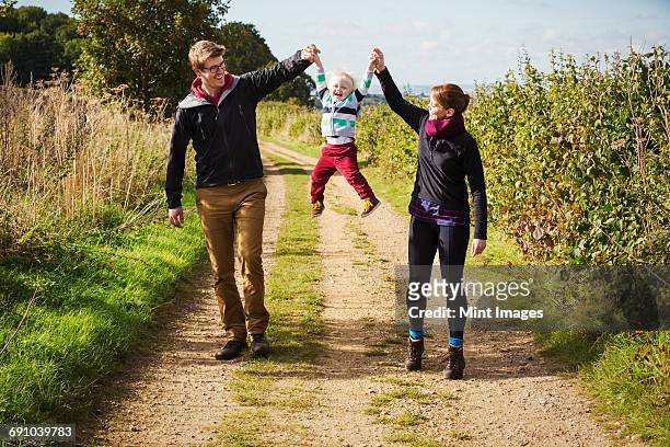 parents holding a small boys hands and lifting him up in the air. - oxfordshire stock pictures, royalty-free photos & images