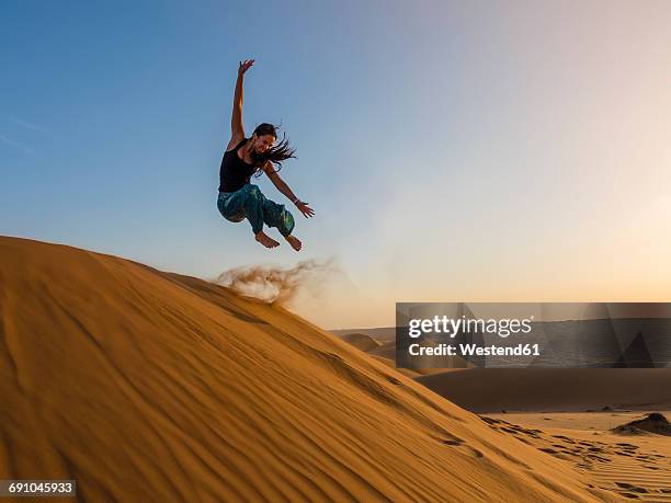 oman, al raka, young woman jumping from dune in rimal al wahiba desert - people from oman stockfoto's en -beelden