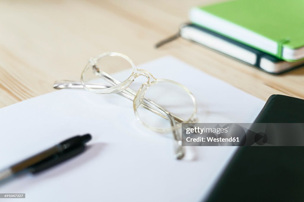 Spectacles on a sheet of paper on desk with notebooks and pen