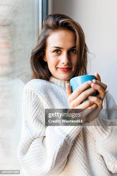 smiling young woman drinking a coffee at a window - heißes getränk stock-fotos und bilder