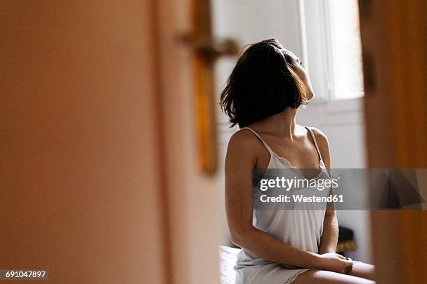 young woman sitting on bed at home looking out of window - door ajar stock pictures, royalty-free photos & images