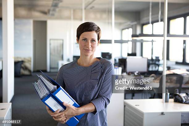 businesswoman in office holding folders - woman waist up stock-fotos und bilder