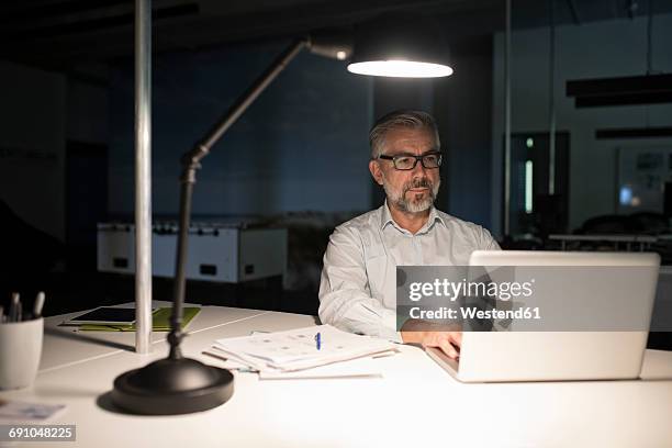 businessman in office using laptop in the dark - schreibtischlampe stock-fotos und bilder