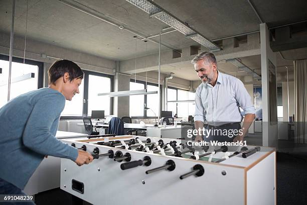 two colleagues playing foosball in office - coworkers having fun stock-fotos und bilder