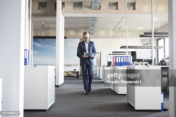 businessman walking in office holding documents - business men walking stock pictures, royalty-free photos & images