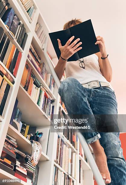 woman reading a book at bookshelf - literature review stock pictures, royalty-free photos & images