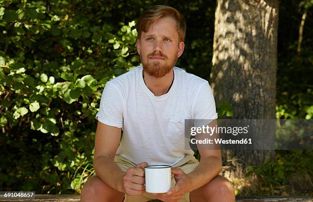 young man holding a mug in nature - emaille stock-fotos und bilder