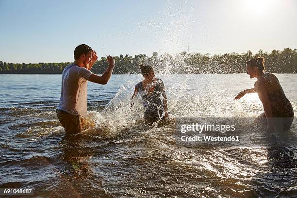 playful friends splashing in a lake - bathing in sunset stockfoto's en -beelden
