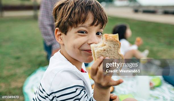 portrait of smiling boy holding sandwich with his family in background - eating sandwich stock-fotos und bilder