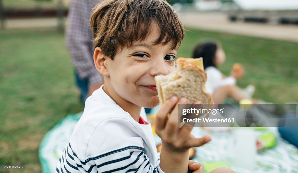 Portrait of smiling boy holding sandwich with his family in background