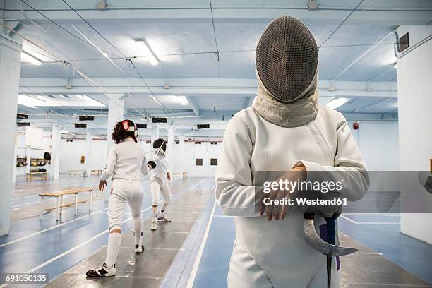 female fencer wearing fencing mask with fencing match in the background - face guard sport stock-fotos und bilder