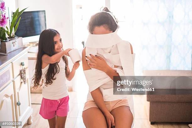 playful teenage girl and her little sister on couch - wrapped in toilet paper stock-fotos und bilder