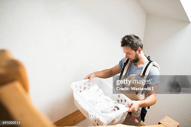 father with baby in baby carrier carrying laundry basket walking upstairs - carrying laundry stock pictures, royalty-free photos & images