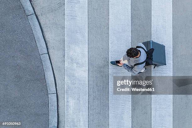 businessman with baggage crossing the street while looking at cell phone, top view - paso de cebra fotografías e imágenes de stock