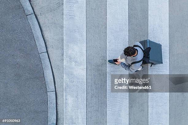 businessman with baggage crossing the street while looking at cell phone, top view - business man technology travel stockfoto's en -beelden