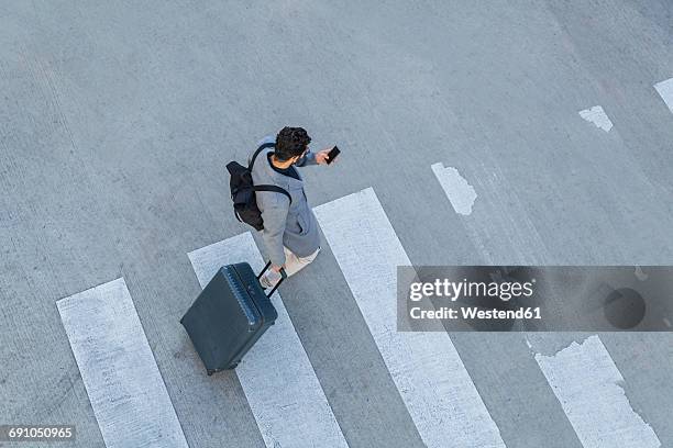 businessman with baggage crossing the street while looking at cell phone, top view - zebrastreifen stock-fotos und bilder