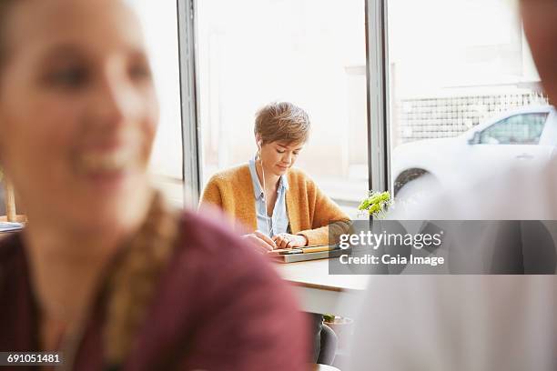 woman with headphones using digital tablet at cafe window - ipad kopfhörer stock-fotos und bilder