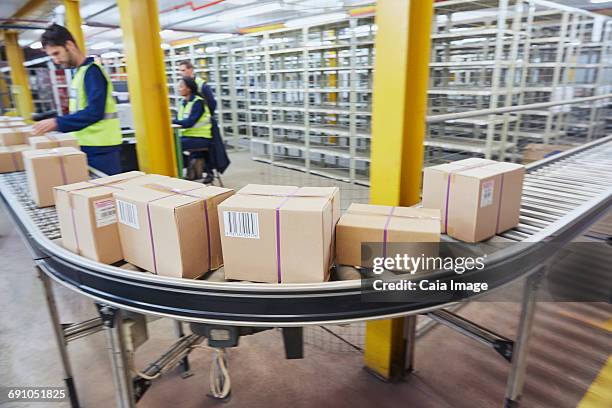 workers processing boxes on conveyor belt in distribution warehouse - boxes conveyor belt stockfoto's en -beelden