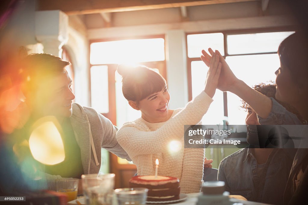 Young friends celebrating birthday with cake and candle high-fiving