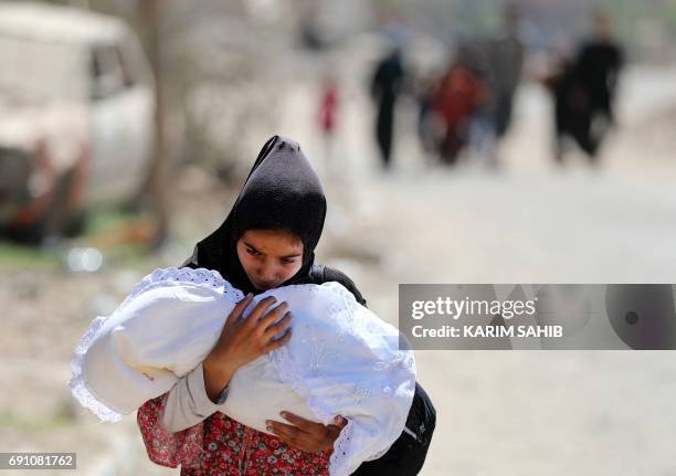 Displaced Iraqi woman carries a baby as she evacuates from western Mosul's Zanjili neighbourhood on June 1, 2017 during ongoing battles between Iraqi...