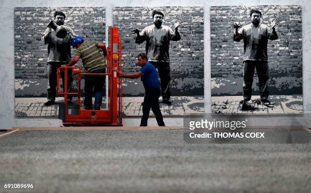 Workers pass art work by Chinese artist Ai Weiwei titled "Dropping a Han Dynasty Urn" which is made with Lego bricks on the eve of the opening of his...