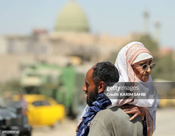 Displaced Iraqi man carries an elderly woman as he evacuates his home in western Mosul's Zanjili neighbourhood on June 1, 2017 during ongoing battles...