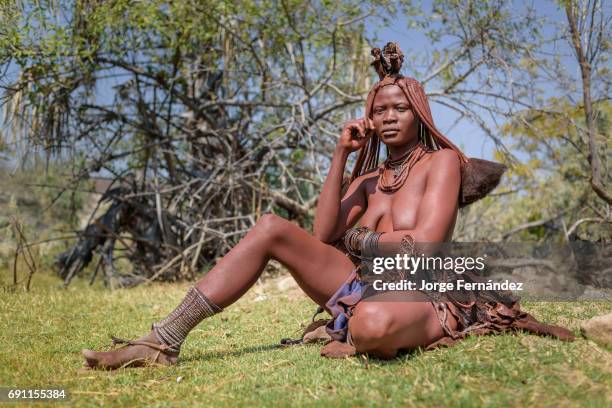 Portrait of a Himba woman sitting on the ground in a small village. Himbas are a bantu tribe who migrated into what today is Namibia a few centuries...