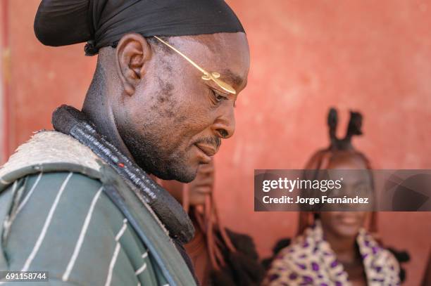 Himba man with traditional himba attires and himba women in the background.