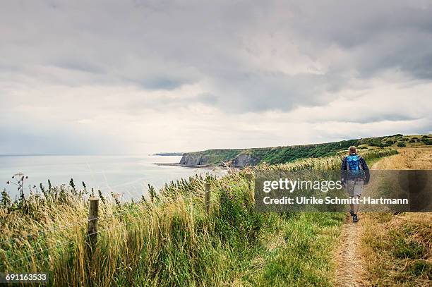 man with bagpack walking along coastal path - bagpack stock pictures, royalty-free photos & images