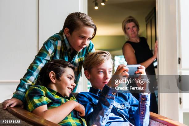 madre con uno sguardo neutro non infelice sul viso guardando i ragazzi che usano internet su un telefono - sospetto foto e immagini stock