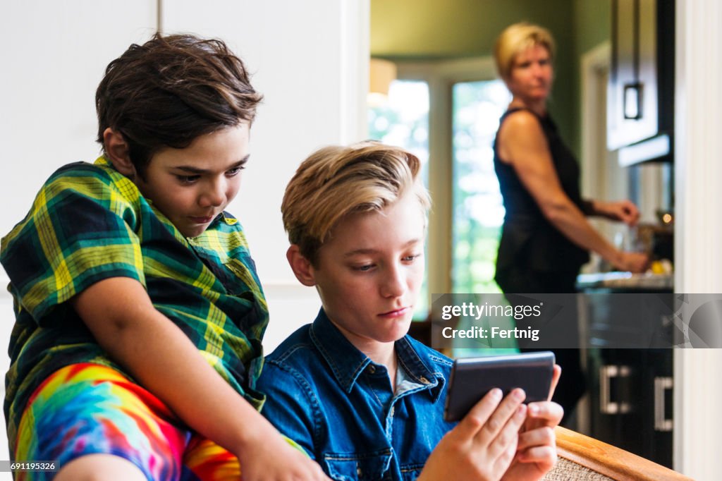 Madre con mirada un poco preocupada en el rostro viendo a niños utilizando internet en un teléfono