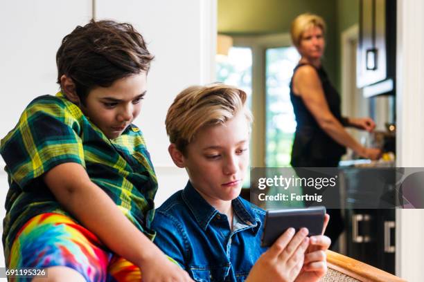 mother with slightly concerned look on her face watching boys using the internet on a phone - children on the internet stock pictures, royalty-free photos & images