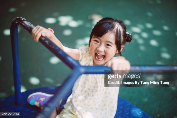 lovely little girl playing on the merry go round in the playground joyfully - playground stock pictures, royalty-free photos & images