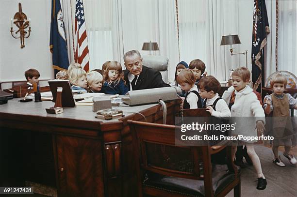 President of the United States, Lyndon B Johnson pictured sitting at the Johnson desk as he gives a group of young children a tour of the Oval Office...